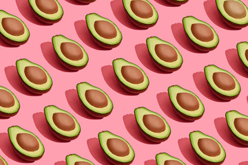 Colorful fruit pattern of fresh cutted avocado halves with pits on coral pink background, top view