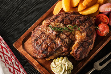 Ribeye steak with potatoes, onions and baked cherry tomatoes. Juicy steak with flavored butter