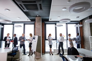 Corporate business team stand with documents in one line on the background of a panoramic window in the office. Ethnic business partners