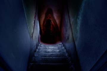 Dark figure in a red cape with a hood on the old concrete stairs in the descent to the basement.