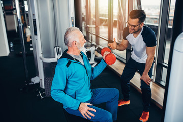 Senior man exercising in gym with his personal trainer.