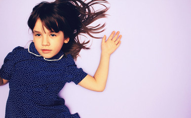 Charismatic child in a blue dress with white polka dots on a color light background. Place for inscription