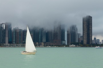 White sailboat on Lake Michigan with Chicago skyscrapers shrouded in fog in the background