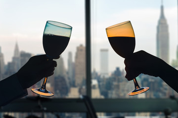 Man and female toasting with glasses of red wine in the apartment with New York city view.