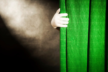 Hand in white glove on a background of green curtains, with the light from the reflector on a black...