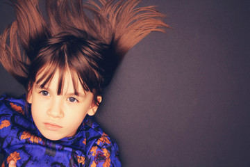 Charismatic girl in a blue dress with abstract orange flowers on a dark background. Place for inscription. child