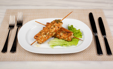 Meat kebab on wooden skewers with a leaf of green lettuce.