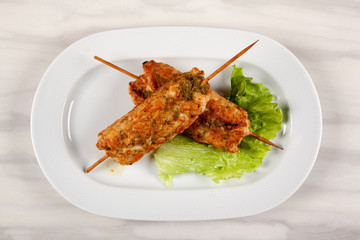 Meat kebab on wooden skewers with a leaf of green lettuce.