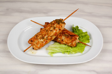 Meat kebab on wooden skewers with a leaf of green lettuce.