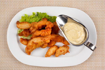 Fried chicken fillet nuggets with sauce on a white plate.