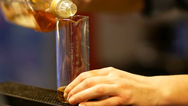 Young barman pouring scotch into the measurable cup. He is preparing an alcohol cocktail.