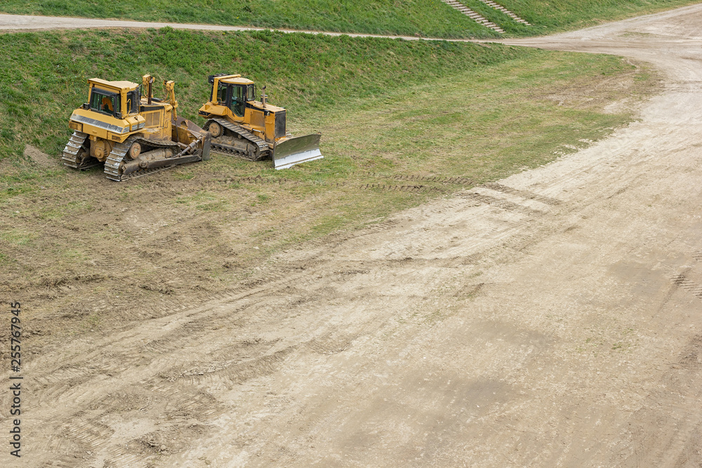 Wall mural two bulldozers parked on a patch of grass by the dirt road on a construction site