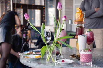 Food stylist and photographer decorate, preparing to shoot various cocktails, milkshakes, smoothies, flower tulips vase on table. Concept professional photography, photosession new menu, freelance