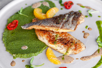 Closeup fried sea bass fillet with green pea puree, tomatoes, sauce, orange slices. Concept professional photography, photosession new menu, profession food stylist, flat-lay, freelancer