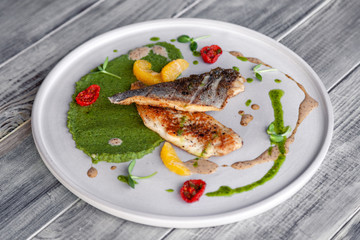 Closeup fried sea bass fillet with green pea puree, tomatoes, sauce, orange slices. Concept professional photography, photosession new menu, profession food stylist, flat-lay, freelancer