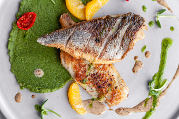Closeup fried sea bass fillet with green pea puree, tomatoes, sauce, orange slices. Concept professional photography, photosession new menu, profession food stylist, flat-lay, freelancer
