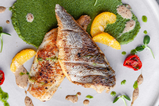 Closeup fried sea bass fillet with green pea puree, tomatoes, sauce, orange slices. Concept professional photography, photosession new menu, profession food stylist, flat-lay, freelancer