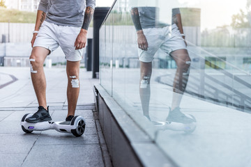 Fototapeta premium Man with sticking bandages on knees standing with one foot on the gyro scooter