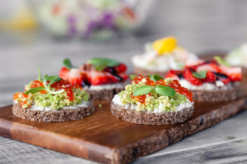 Сloseup macro set of different northern trendy appetizers on smorrebrod rye bread with red caviar and avocado, strawberries, balsamic dressing. Concept quick snack in wine bar, food shooting