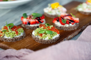 Сloseup macro set of different northern trendy appetizers on smorrebrod rye bread with red caviar and avocado, strawberries, balsamic dressing. Concept quick snack in wine bar, food shooting