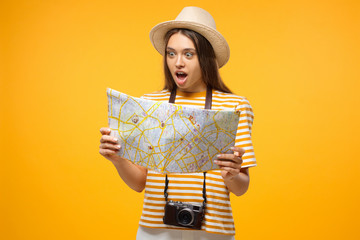 Surprised young woman tourist looking at paper map with mouth open, isolated on yellow background