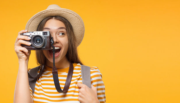 Tourism concept. Horizontal banner of excited young woman tourist holding photo camera, isolated on yellow background with copy space