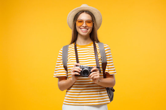 Travel concept. Young smiling woman tourist holding photo camera, isolated on yellow background.