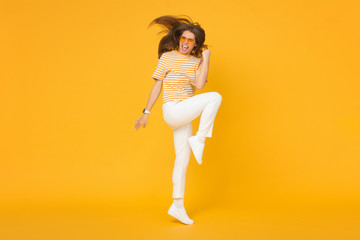 Fototapeta na wymiar Happy active girl jumping in the air if she is a winner, isolated on yellow background
