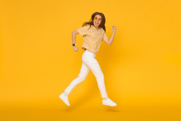 Fototapeta na wymiar Happy funny sporty girl jumping like she walking in the air, isolated on yellow background