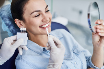 Männlicher Zahnarzt vergleicht die Farbe der Zähne der Dame mit der Probe