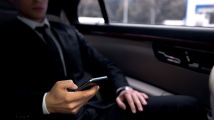 Successful businessman in luxury auto, scrolling smartphone, reading e-mail app