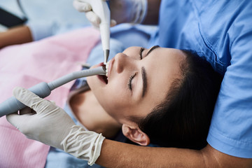 Obraz na płótnie Canvas Young lady with closed eyes having dental procedure at modern clinic