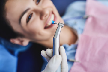 Male dentist holding instrument for teeth cleaning while young lady smiling