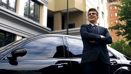 Happy young male standing by new luxurious car, office worker getting promotion