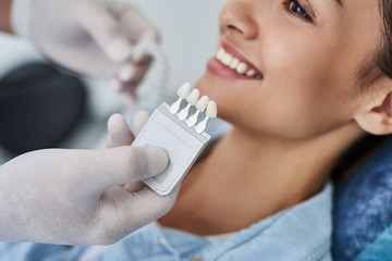 Dentist choosing color of teeth for young woman