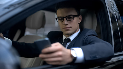 Serious businessman testing new business app on telephone while waiting in car