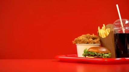Fried wings french fries hamburger and soda drink on red tray, takeaway food