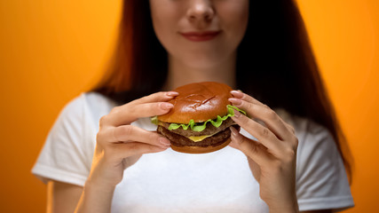Girl looking at burger, enjoying fast food, high calorie nutrition, obesity risk