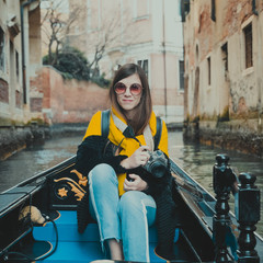 Fototapeta na wymiar A young woman enjoys a gondola ride and making photo in the canals of Venice. 