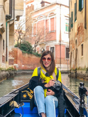Fototapeta na wymiar A young woman enjoys a gondola ride and making photo in the canals of Venice. 