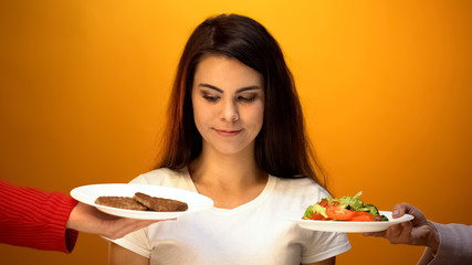 Young girl choosing between cutlets and vegetarian salad, complicated choice