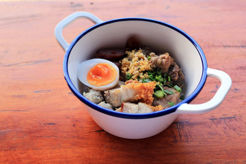 Thai rice porridge breakfast served with topping such as pork meatballs, fried onions, garlic, egg, green onions, and cilantro.