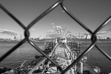 Abstract abandoned snow covered pier. Pier with city water lake background. Looking through chain link gate fence. Abstract industrial design and detail. Seagulls on pier.