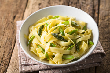 Fresh homemade pasta dish of fettuccine or tagliatelle, green asparagus, garlic and lemon juice in bowl (Selective Focus, Focus on the asparagus head in the middle)