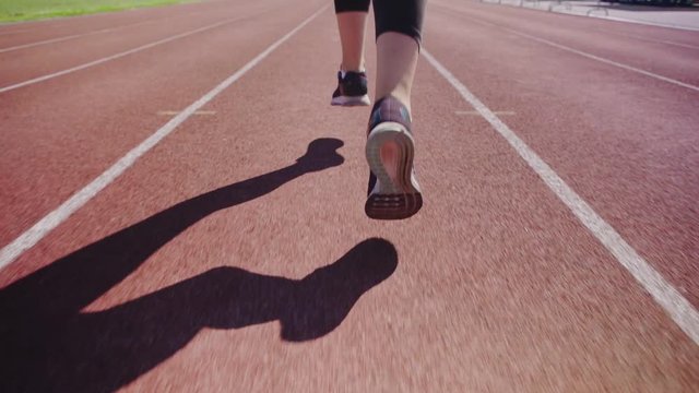 Close-up feet of unrecognizable female athlete running on track in slow motion