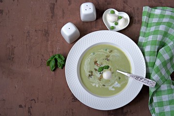 Cream of green pea soup, sprinkled with pumpkin seeds, in a white plate. Served with mozzarella cheese. Top view.