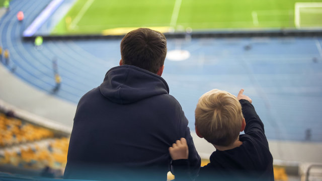 Boy With Older Brother Watching Football Team Training At Empty Stadium, Fans