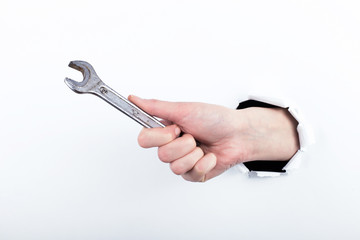 Female hand out of a hole in paper, holds a wrench. Isolate on white background to labor day.