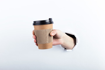 Female hand out of the hole in the paperman, keeps a brown glass of coffee with him. Isolate on white background.