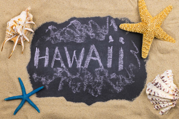 Handwritten word HAWAII written in chalk, among seashells and starfishes.